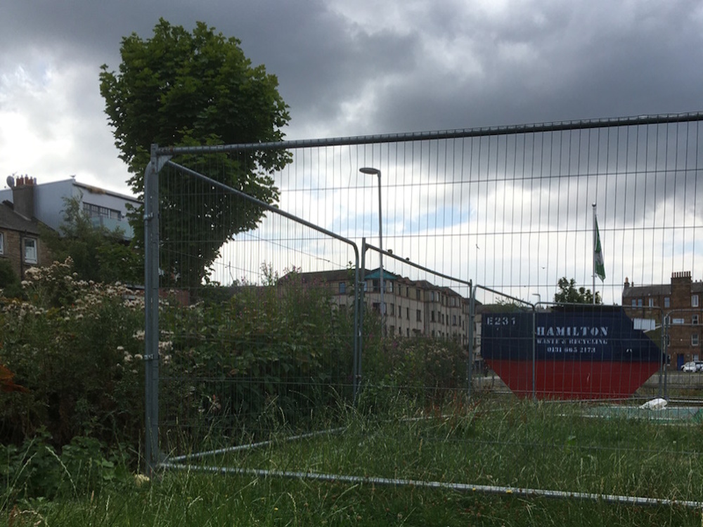 Overgrown grass lawn with fence and skip 
