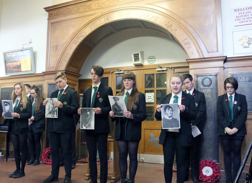 Boroughmuir pupils displaying photographs of war casualties standing in front of the school's memorial arch