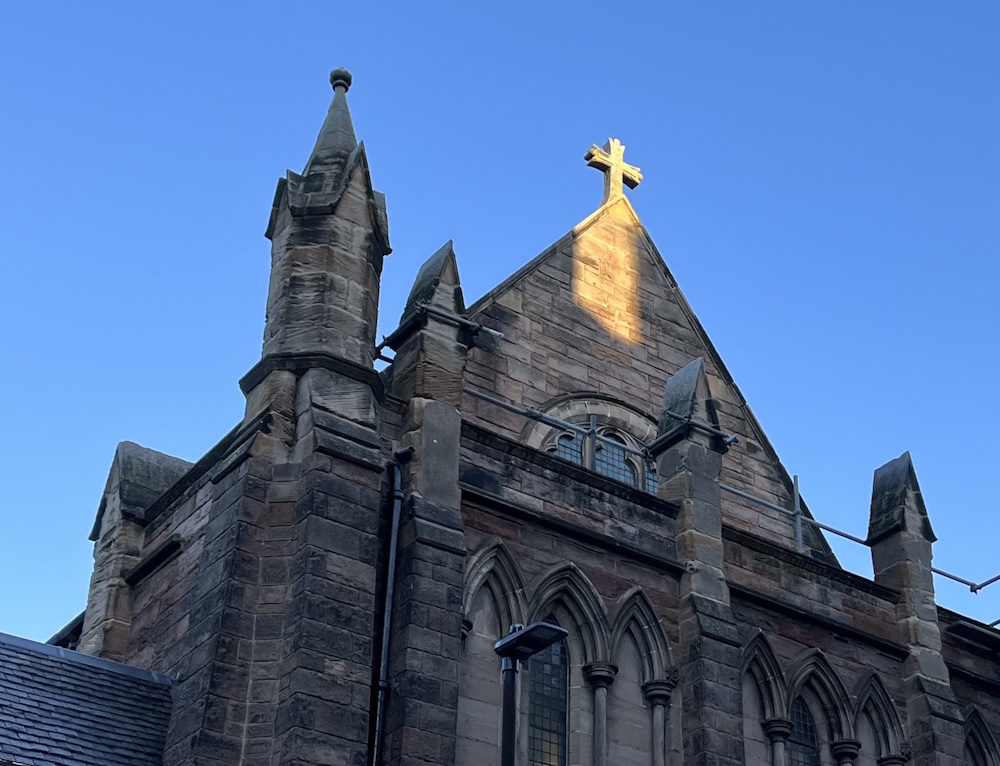 Sun shining on the croos on top of St. Oswalds church hall 